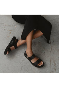 black vegan leather sandals - the dorothy, edie collective - worn against concrete background